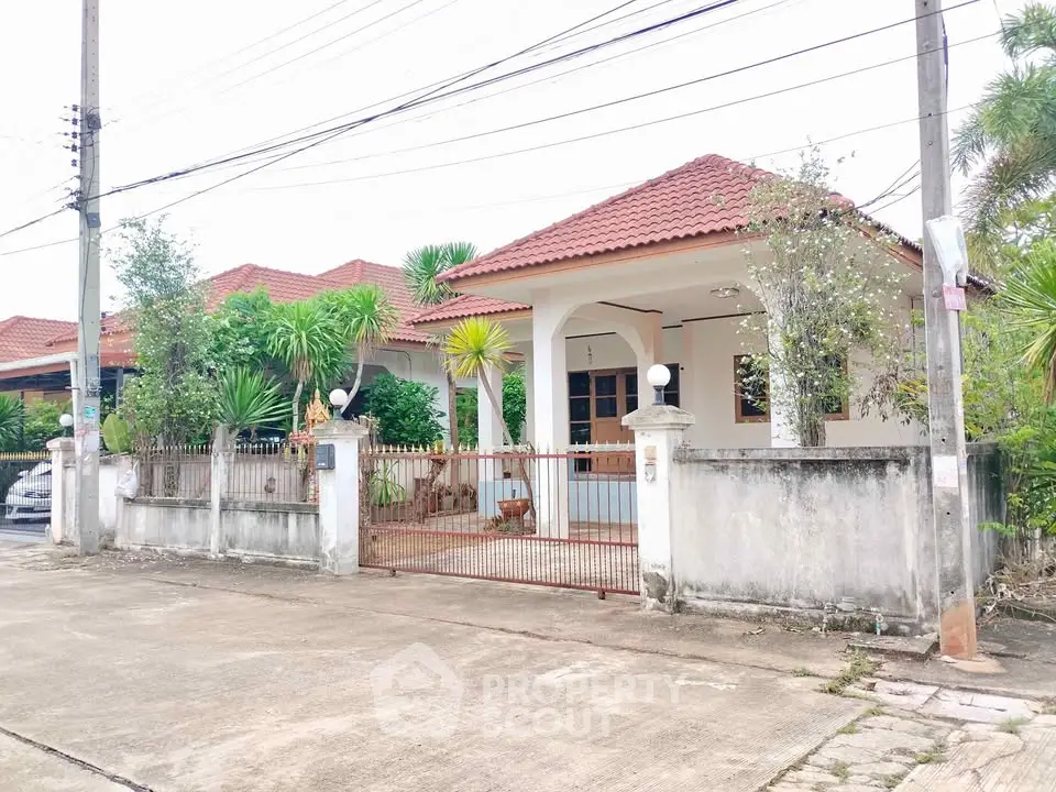 Charming single-story house with red-tiled roof and lush greenery in a serene neighborhood.