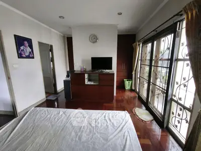 Spacious bedroom with large windows and wooden flooring, featuring a TV and elegant decor.