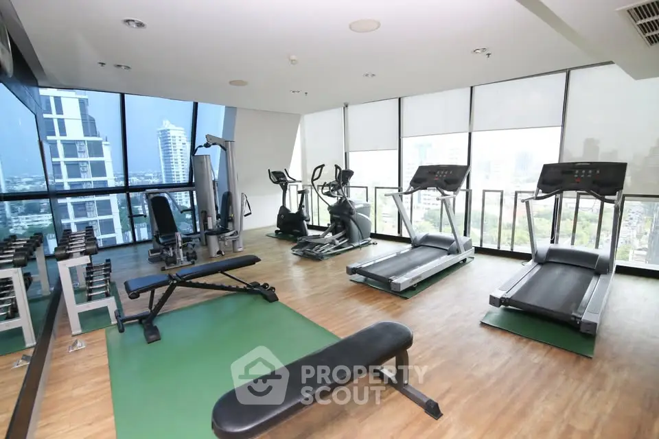 Modern gym with city view featuring treadmills and weights in a high-rise building.