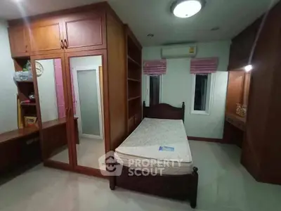 Spacious bedroom with built-in wooden wardrobe and cozy single bed, perfect for comfortable living.