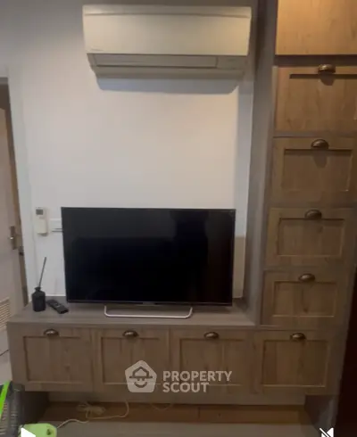 Modern living room with TV and wooden cabinetry under air conditioning unit.