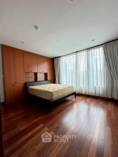 Spacious bedroom with wooden flooring and large windows for natural light.