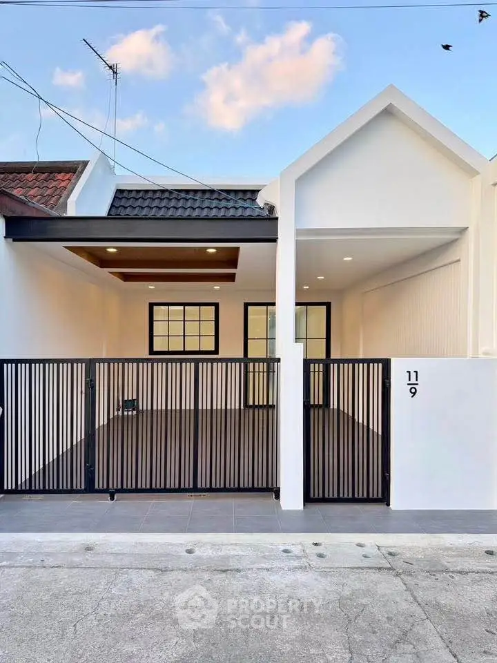Modern minimalist house exterior with sleek black gate and white facade under a clear blue sky.