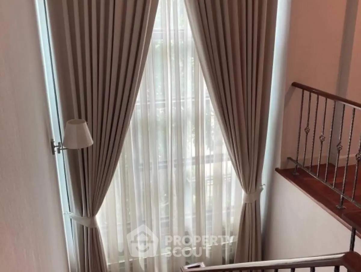 Elegant staircase with tall window and luxurious curtains in a modern home.