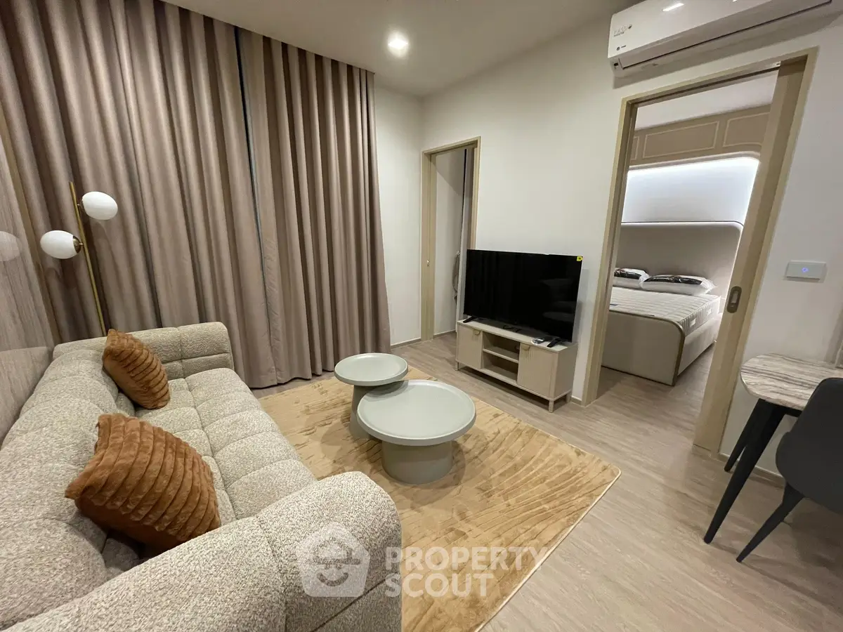 Modern living room with cozy sofa, stylish decor, and view into elegant bedroom.
