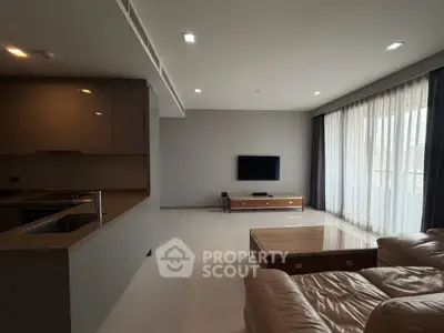 Modern living room with sleek furniture and open kitchen layout, featuring a cozy leather sofa and wall-mounted TV.