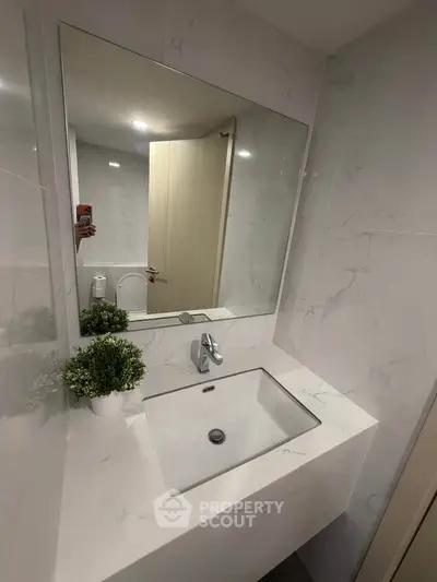 Modern bathroom with sleek white sink and large mirror, featuring elegant marble walls and stylish decor.