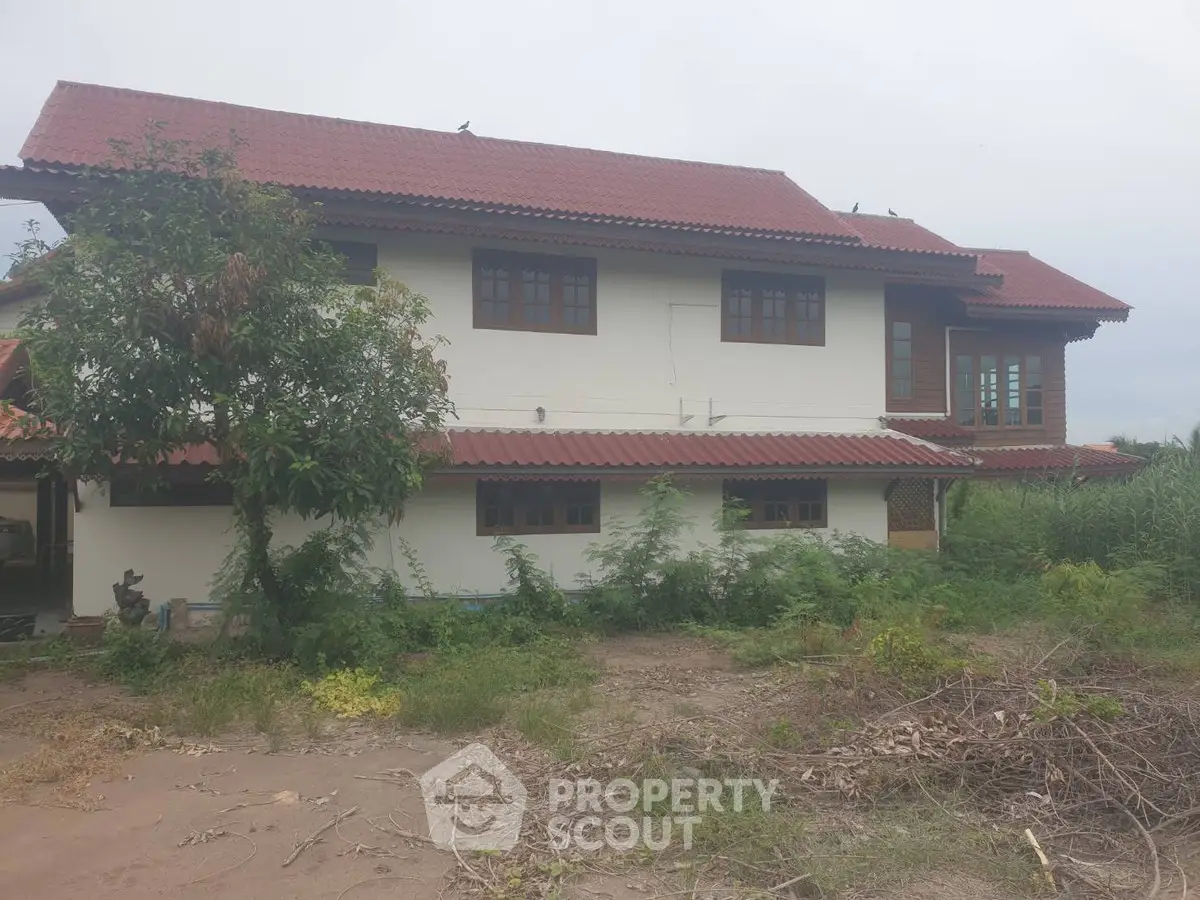 Charming two-story house with red-tiled roof and lush greenery, perfect for serene living.