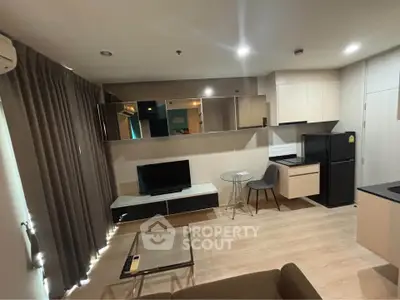 Modern living room with sleek design, featuring a TV, glass coffee table, and compact kitchen area.