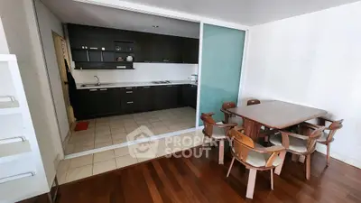 Modern kitchen with dark cabinets and dining area with wooden table and chairs.