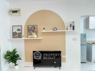 Modern living room with stylish decor and wall-mounted shelves, featuring a flat-screen TV and a glimpse of the kitchen.