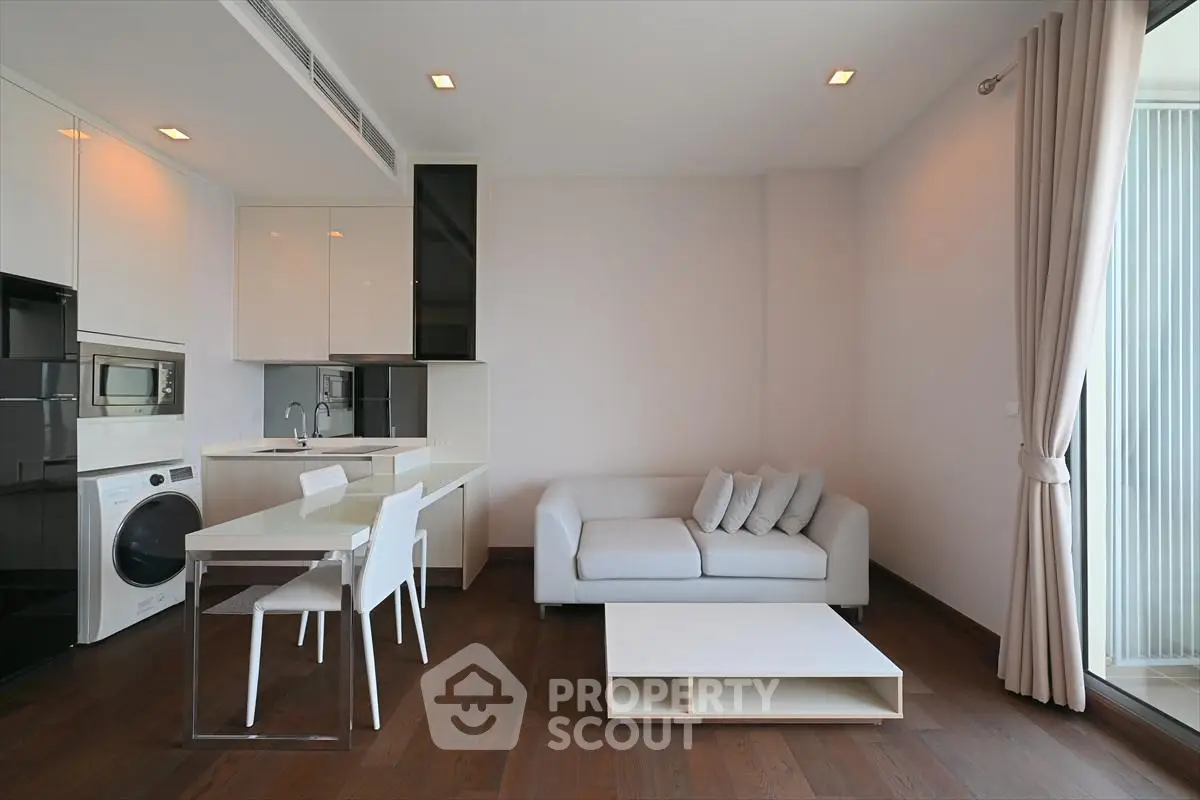 Modern living room with sleek kitchen, white sofa, and dining area in open layout apartment.