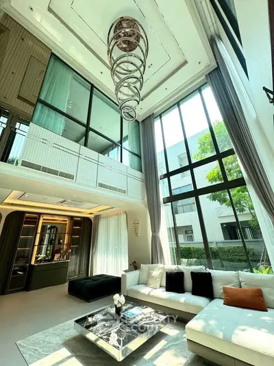 Luxurious living room with high ceilings and modern chandelier, featuring large windows and elegant decor.