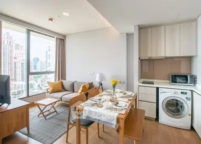Modern open-plan living room with city view, featuring cozy seating and dining area with washing machine.