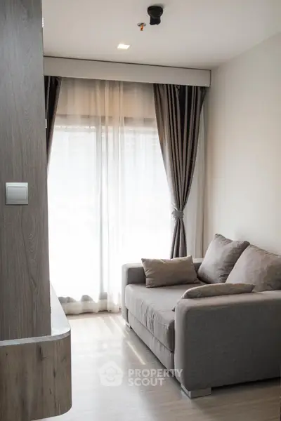 Cozy living room with modern sofa and large window draped with elegant curtains, perfect for relaxation.