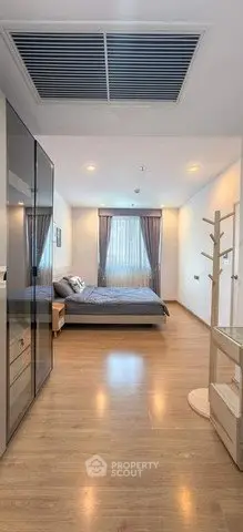 Spacious modern bedroom with wooden flooring and large window for natural light.