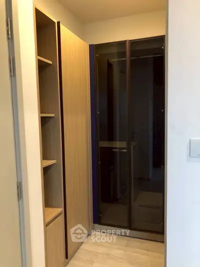 Modern walk-in closet with sleek wooden shelves and glass doors in a stylish apartment.
