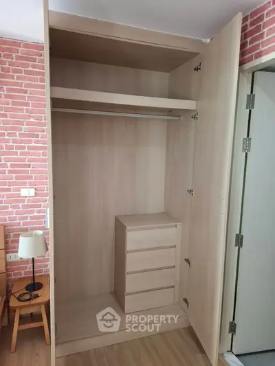 Spacious wooden wardrobe with built-in drawers in modern bedroom with brick accent wall.
