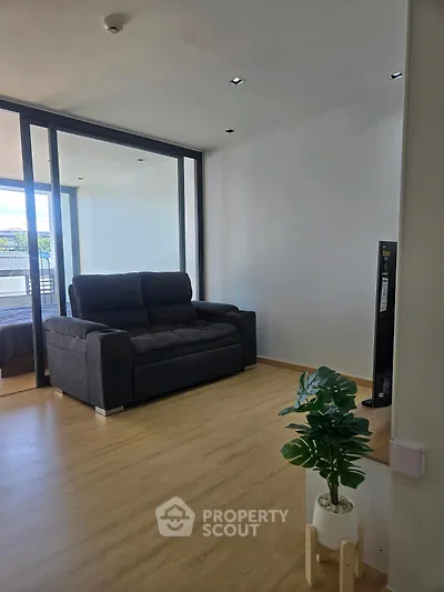 Modern living room with sleek black sofa and wooden flooring, featuring a large glass door leading to a balcony.