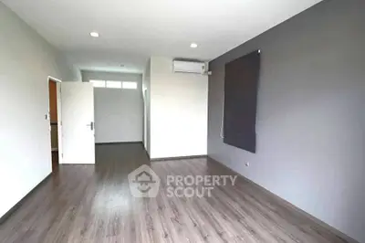 Spacious empty room with wooden flooring and air conditioning, ready for customization.