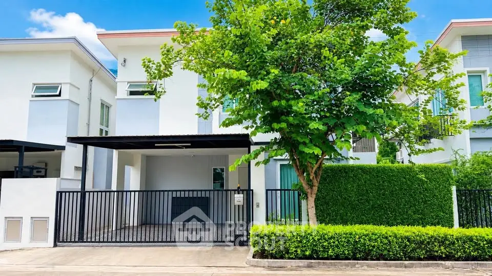 Modern two-story house with gated driveway and lush greenery in a serene neighborhood.