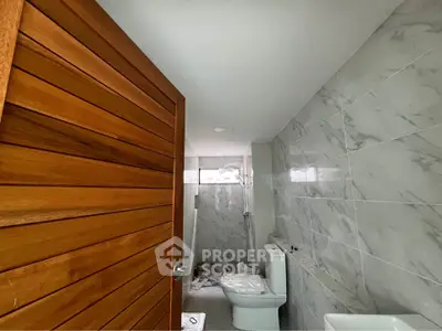 Modern bathroom with marble tiles and wooden door, featuring a sleek toilet and shower area.