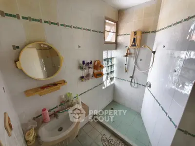 Cozy bathroom with shower and sink, featuring tiled walls and natural light.