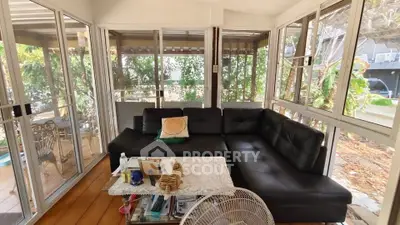 Spacious sunroom with black leather sectional and garden view, perfect for relaxation and entertaining.
