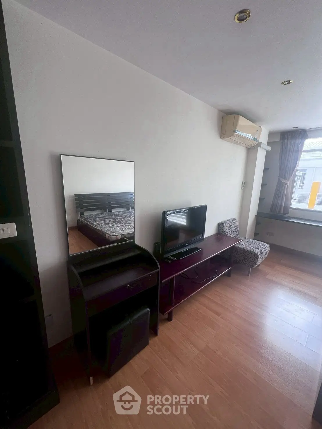 Cozy bedroom with modern furniture and natural light, featuring a TV and air conditioning.