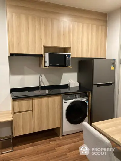 Modern kitchen with wooden cabinets, sleek black countertop, and integrated appliances including a fridge and microwave.