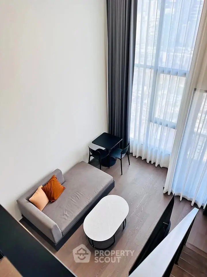 Modern living room with high ceilings and large windows offering city views.