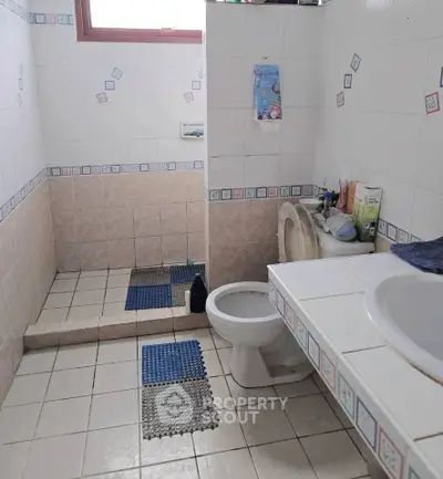 Spacious bathroom with tiled walls and floor, featuring a toilet and sink.