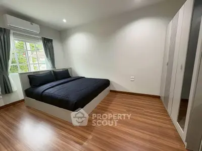 Modern bedroom with sleek wooden flooring and large window for natural light.