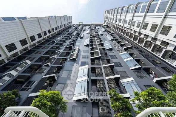 Modern high-rise building with unique geometric facade and lush greenery at the base.