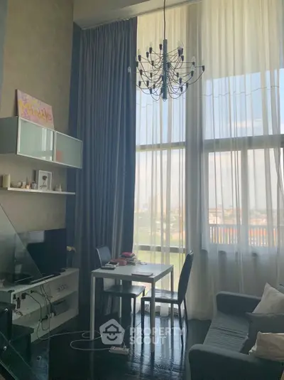 Modern living room with high ceilings, large windows, and elegant chandelier, offering a bright and airy atmosphere.