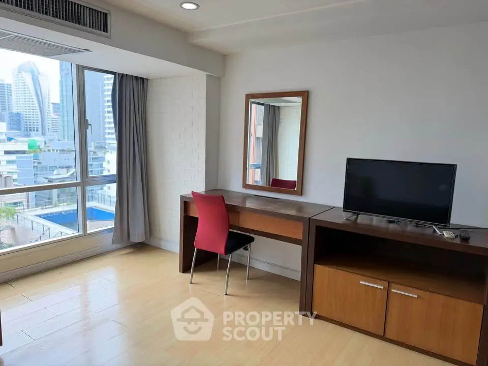Modern apartment interior with city view, featuring a desk, chair, and TV setup.