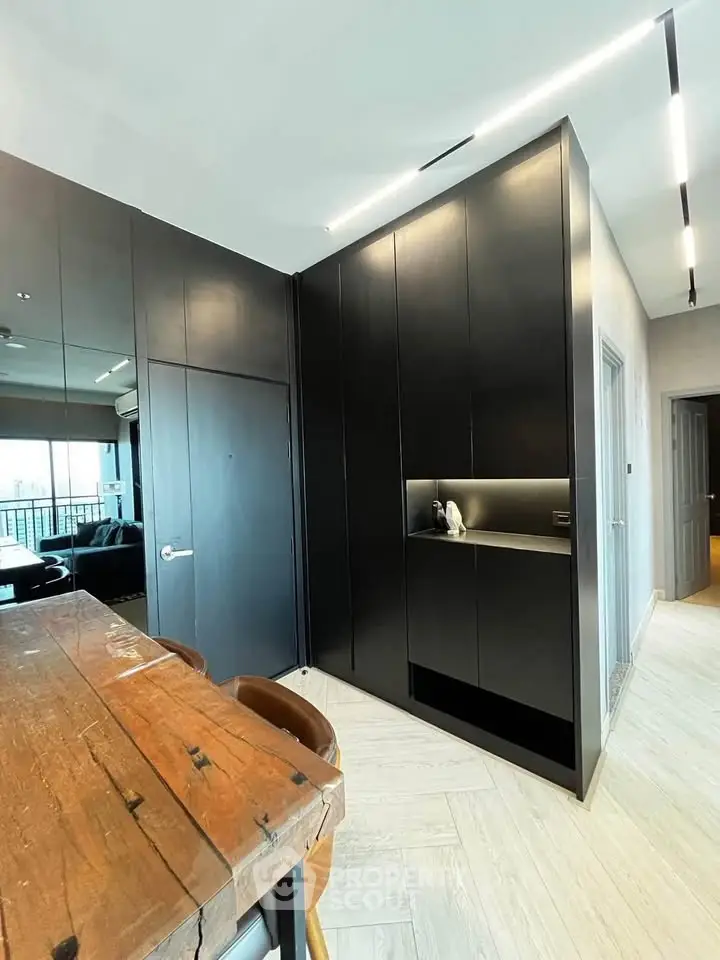 Modern kitchen with sleek black cabinetry and rustic wooden dining table in stylish apartment.