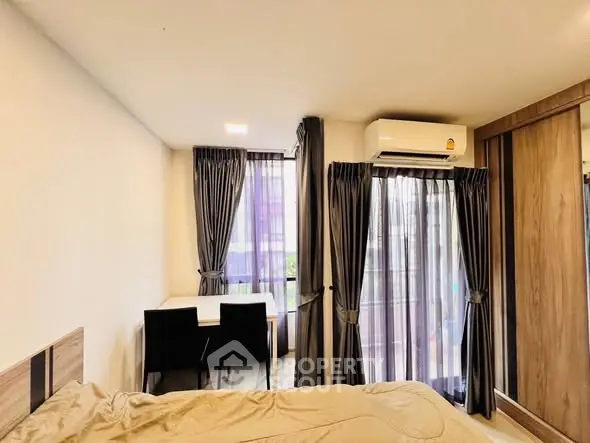 Modern bedroom with large windows and stylish curtains, featuring a cozy bed and a small dining area.