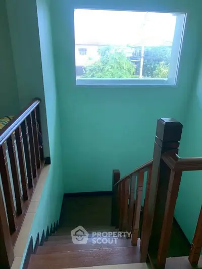 Charming staircase with wooden railing and large window offering natural light and outdoor view.