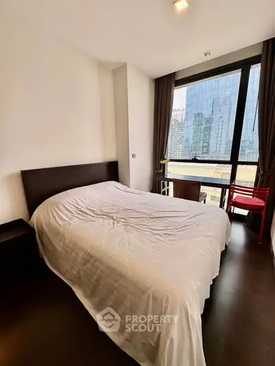 Modern bedroom with city view, featuring sleek furniture and large window for natural light.
