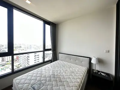 Modern bedroom with large windows offering a stunning city view, featuring a comfortable bed and sleek nightstand.