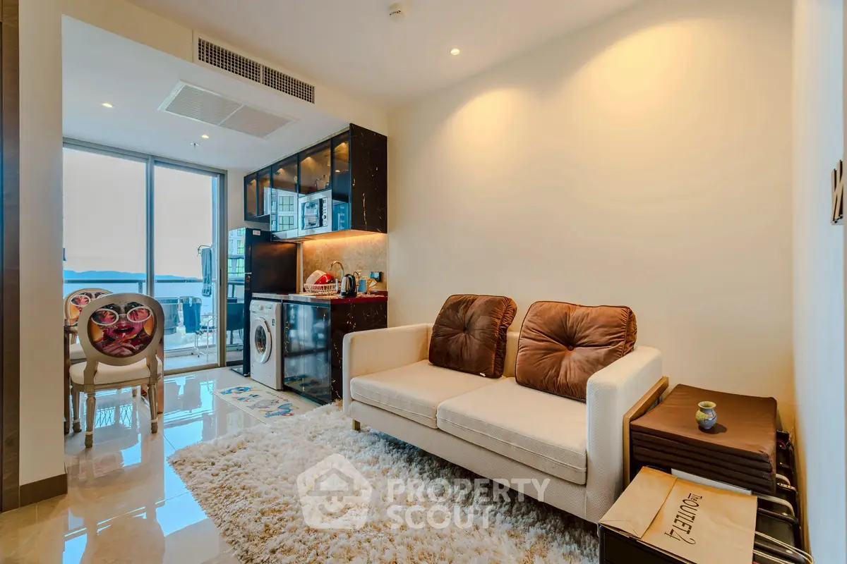 Modern living room with cozy sofa, plush rug, and open kitchen layout with ocean view.