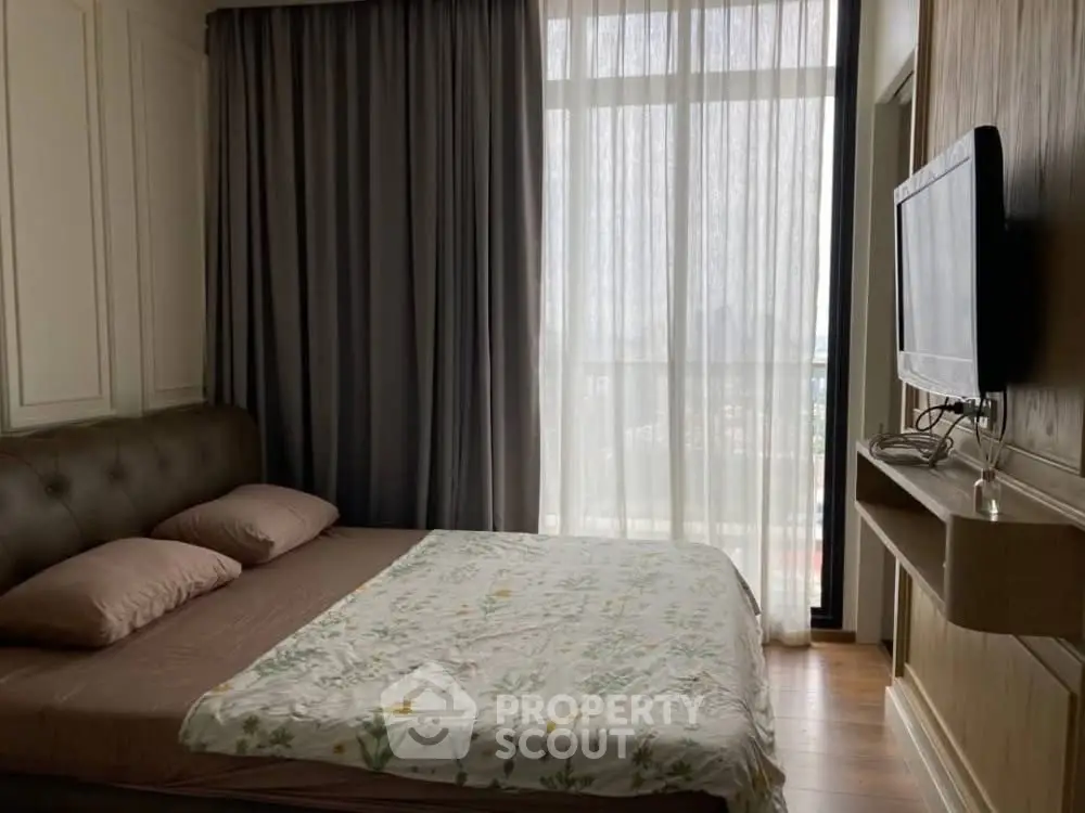 Cozy bedroom with large window and wall-mounted TV, perfect for relaxation.