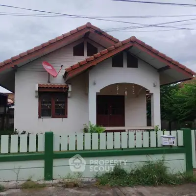 Charming single-story house with red roof and green fence, perfect for cozy living.