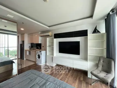 Modern living room with sleek design, featuring built-in TV unit, washing machine, and open kitchen layout.