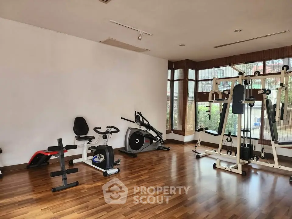 Spacious gym with modern exercise equipment and wooden flooring in a bright, well-lit room.
