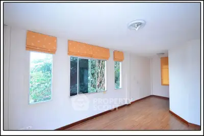 Spacious room with large windows and wooden flooring, offering a serene view of lush greenery.