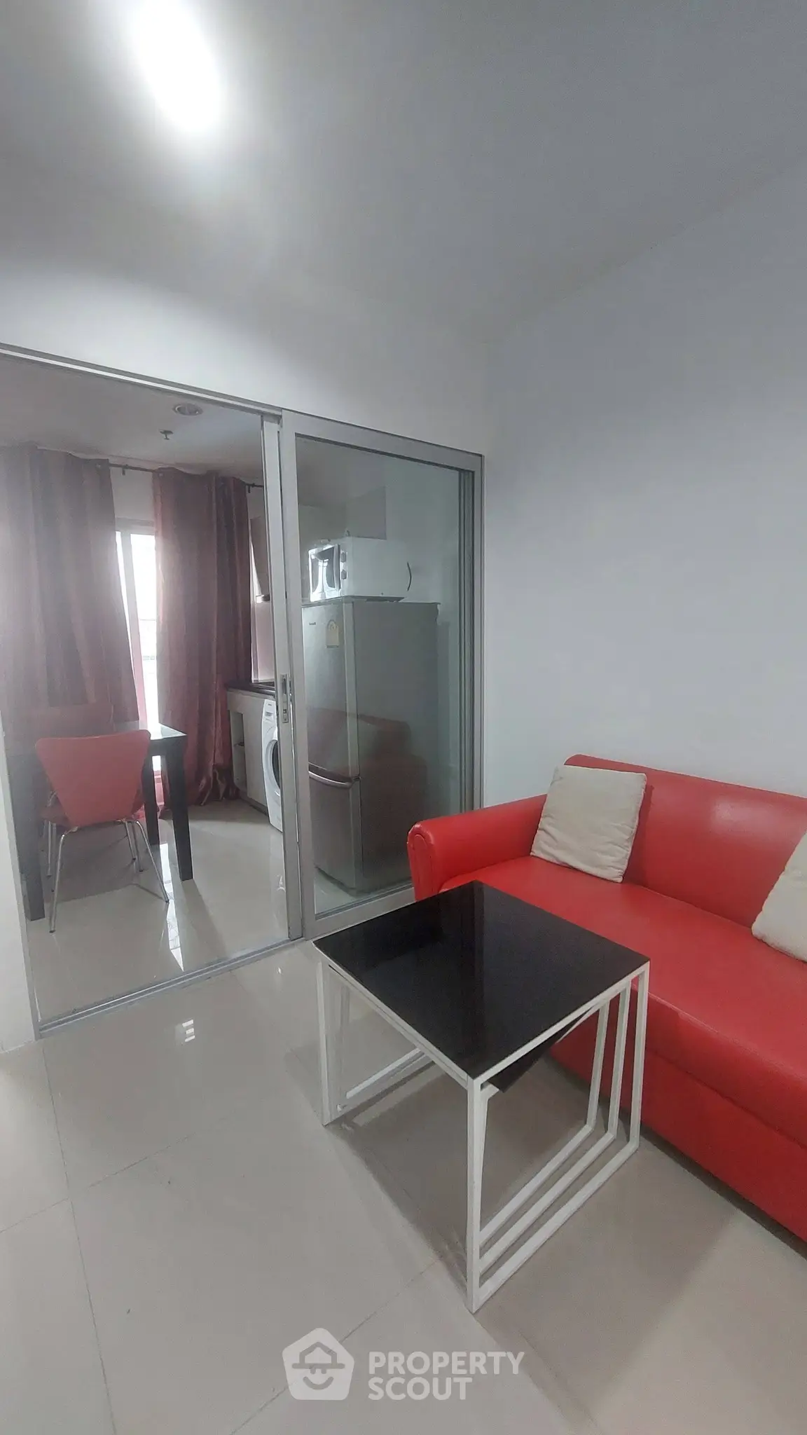 Modern living room with red sofa and glass partition leading to dining area.