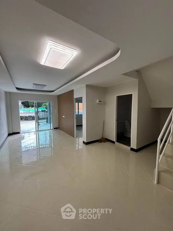 Spacious modern living room with glossy tiled floors and staircase, ideal for family gatherings.
