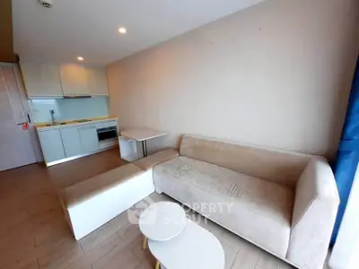 Modern living room with beige sofa and compact kitchen in open layout apartment.